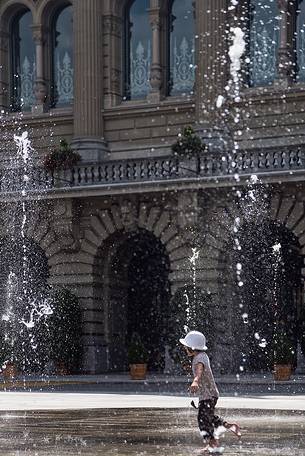 Child playing in the fountain in front of the parliament building in Bern, Switzerland, Europe