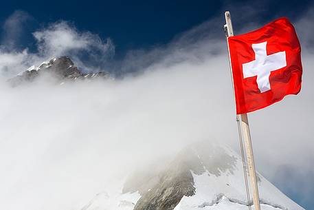 Swiss flag on top of Jungfraujoch , the highest railway station in the Alps, in the background the Jungfrau peak,  Bernese alps, Switzerland, Europe