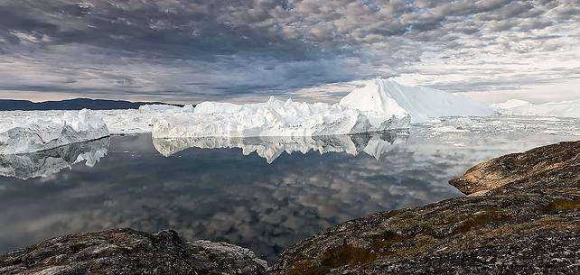 Morning light on icebergs and their reflection on water of Kangerlua Fjord at dawn Morning light on icebergs and their reflection on water of Kangerlua Fjord at dawn