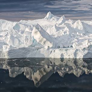 Morning light on icebergs and their reflection on water of Kangerlua Fjord at dawn Morning light on icebergs and their reflection on water of Kangerlua Fjord at dawn