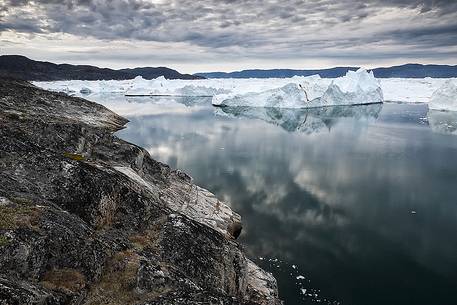 Morning light on icebergs and their reflection on water of Kangerlua Fjord at dawn