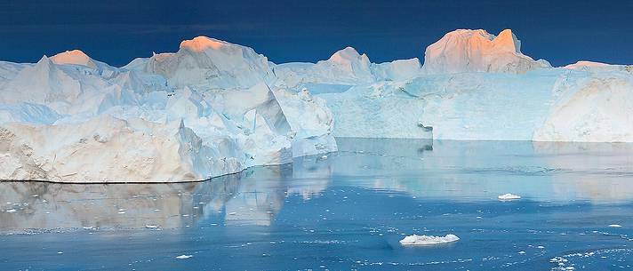 Morning light on icebergs and their reflection on water of Kangerlua Fjord at dawn Morning light on icebergs and their reflection on water of Kangerlua Fjord at dawn