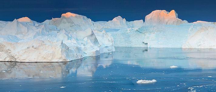 Morning light on icebergs and their reflection on water of Kangerlua Fjord at dawn