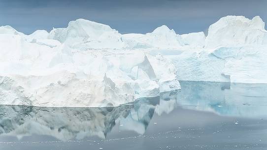 Morning light on icebergs and thei reflection on water of Kangerlua Fjord at dawn