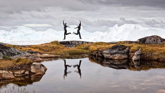 Hiking and action near a small pond; in the background icebergs in Kangerlua Fjord Hiking and action near a small pond; in the background icebergs in Kangerlua Fjord
