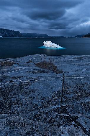 Dark clouds above iceberg in the sea in front  of Ataa a small village of fishermen and seal hunters which was abandoned in the 50s