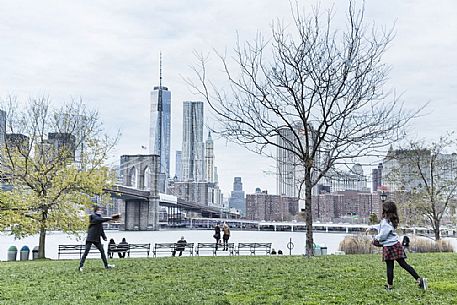 Mother and child relaxing playing baseball; in the background the famous Manhattan skyline with Brooklyn bridge