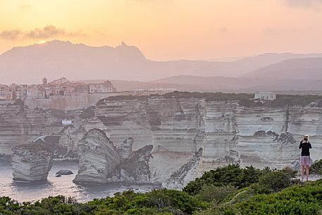 Aa young woman photographs the village of Bonifacio at sunset