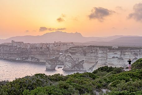 Aa young woman photographs the village of Bonifacio at sunset