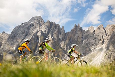 A young mountain bikers come down from Biscia summit, in the background the Sesto Dolomites, Cadore, Italy