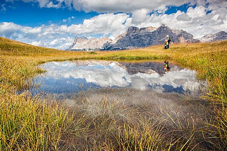 Hikers at lake in Pralongi meadows, in background the Sasso della Croce mountain, Val Badia, Dolomites, South Tyrol, Italy 