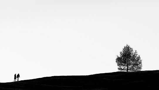 Silhouette coupe hiking along a path of Prati dell'Armentara, South Tyrol, Dolomites, Italy 