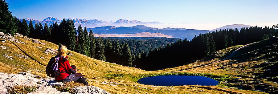 Trekker looking the landscape of  Meletta di Gallio and in the background the dolomites, Asiago, Italy