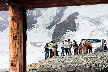 Landscape and tourists reflected from glass of Diavolezza hut admiring the glacier of Bernina mountain range, Pontresina, Engadin, Canton of Grisons, Switzerland, Europe