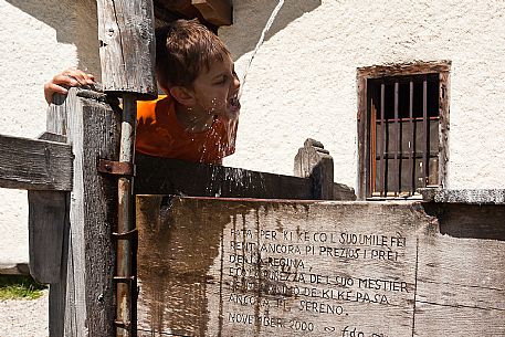 Little boy drinking from a water fountain at the Ombretta alm, Marmolada mountain group, Rocca Pietore, dolomites, Veneto, Italy, Europe