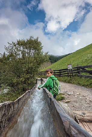 Child plays with natural water that flow in the traditional wooden canal near a water mill, Longiarù, Badia valley, dolomites, Trentino Alto Adige, Italy, Europe Child plays with natural water that flow in the traditional wooden canal near a water mill, Longiarù, Badia valley, dolomites, Trentino Alto Adige, Italy, Europe