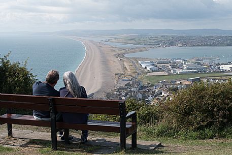 Couple adminirg the panorama from Portland Heights, beautiful viewpoint located on the way to the famous Portland Bill. From Portland Heights you can admire the 17 miles long Chesil beach, also known as Chesil Bank, Dorset, England, UK