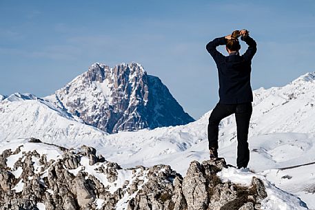 A hiker stops on the crest of Mount Bolza in the plateau of Campo Imperatore to admire the Gran Sasso peak, Gran Sasso national park, Abruzzo, Italy, Europe.