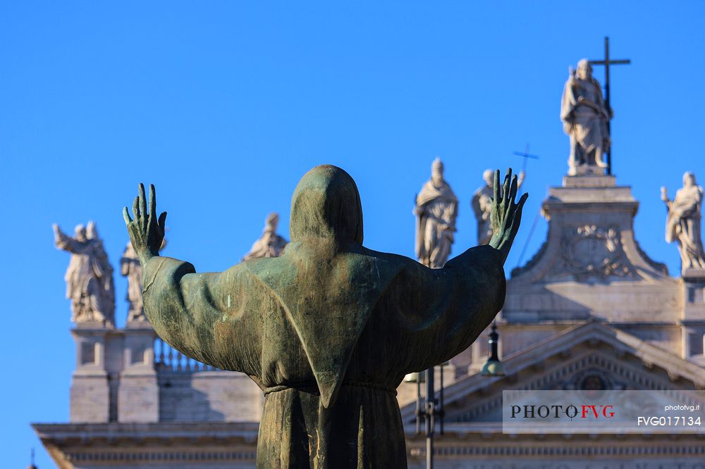 Rome: bronzy statue of St. Francis with the Basilica of St. Giovanni in Laterano on the background