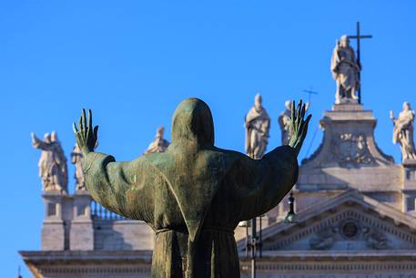 Rome: bronzy statue of St. Francis with the Basilica of St. Giovanni in Laterano on the background