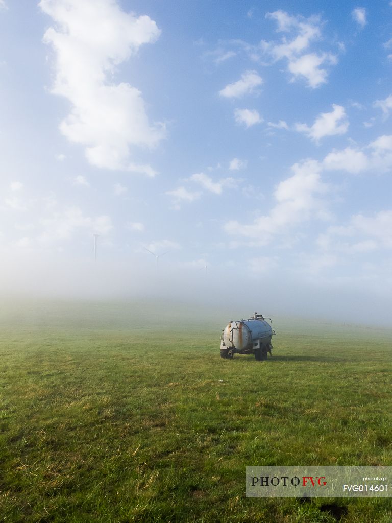 An agricultural machine in a field surrounded by the fog in the early morning