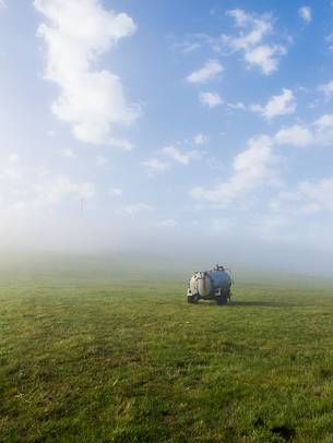 An agricultural machine in a field surrounded by the fog in the early morning