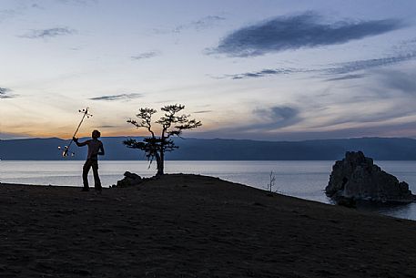 A boy dancing and playing with fire during the sunset at Olkhon Island. In the background the holy Shamanka or Shaman's Rock, Bajkal lake, Russia