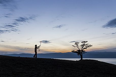 A boy dancing and playing with fire during the sunset at Olkhon Island, Bajkal lake, Russia A boy dancing and playing with fire during the sunset at Olkhon Island, Bajkal lake, Russia