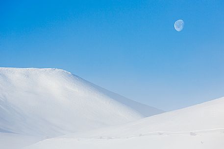 The moon rises in Castelluccio di Norcia in winter, Sibillini National Park, Umbria, Italy, Europe