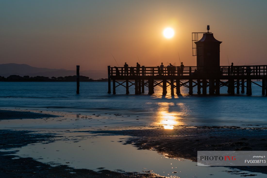 Fishermen in silhouette at the lighthouse of Lignano Sabbiadoro at sunset, Adriatic coast, Friuli Venezia Giulia, Italy, Europe