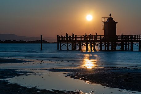 Fishermen in silhouette at the lighthouse of Lignano Sabbiadoro at sunset, Adriatic coast, Friuli Venezia Giulia, Italy, Europe