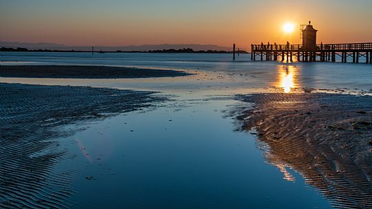 Fishermen in silhouette at the lighthouse of Lignano Sabbiadoro at sunset, Adriatic coast, Friuli Venezia Giulia, Italy, Europe