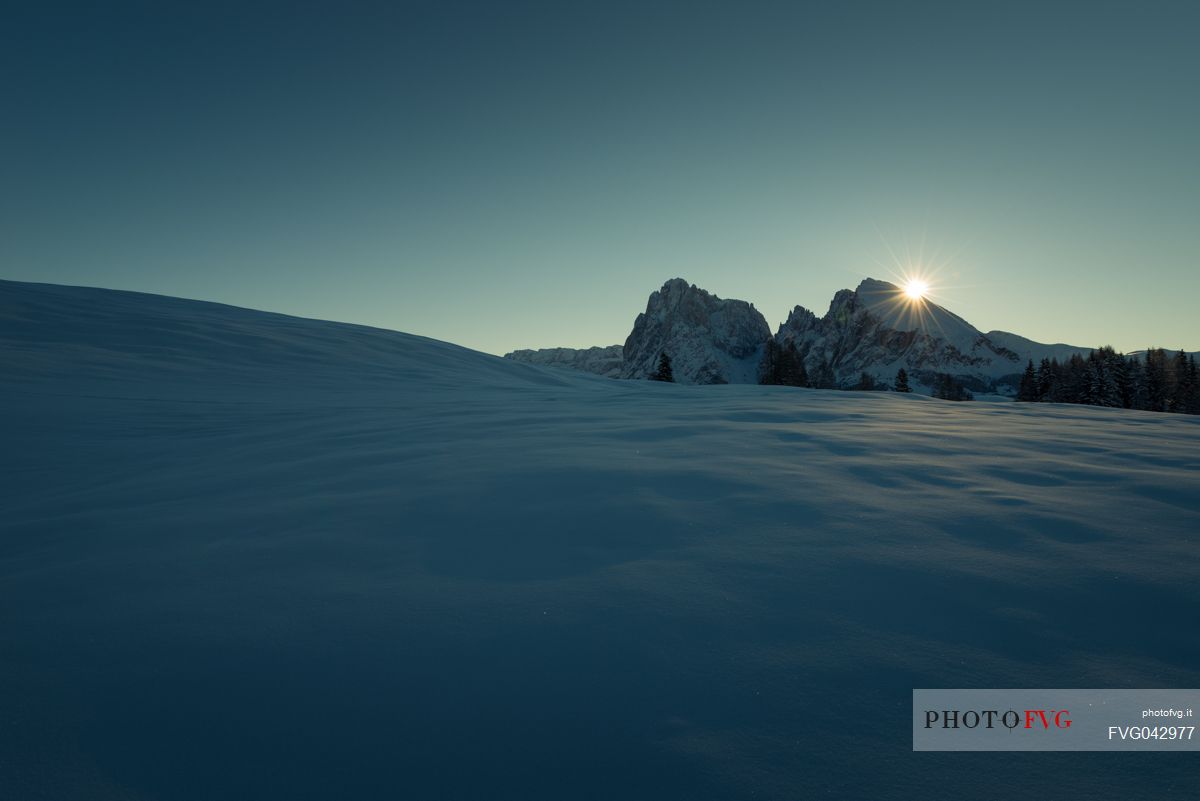 The Seiser Alm covered by the snow still shrouded in shadow while the sun rises behind the Sasso Lungo and the Sasso Piatto, dolomites, South Tyrol, Italy, Europe