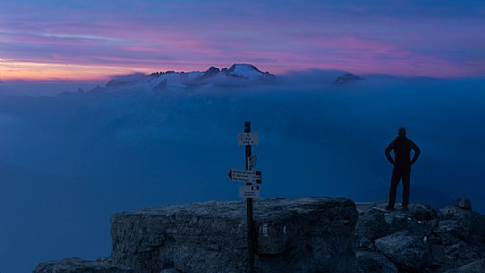 A mountaineer standing up in front of the Marmolada waiting for the sunrise in a cloudy day, Piz Bo, dolomites, Canazei, Trentino Alto Adige, Italy, Europe