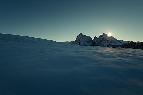 The Seiser Alm covered by the snow still shrouded in shadow while the sun rises behind the Sasso Lungo and the Sasso Piatto, dolomites, South Tyrol, Italy, Europe