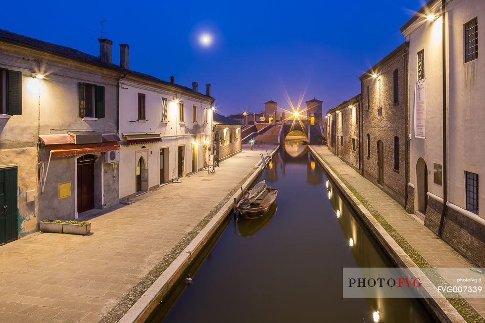 Evening view of a small centre's river and Tre Ponti bridge in the moonlight