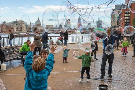 Some children play with big soap bubbles in a little square on the south river of Thames