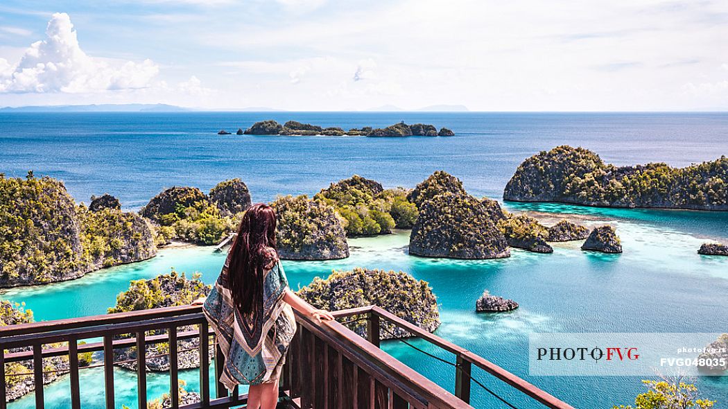 Woman enjoying the landscape from the scenic viewpoint in Piaynemo, one of the Raja Ampat archipelago most popular tourist spots, West Papua, New Guinea, Indonesia.