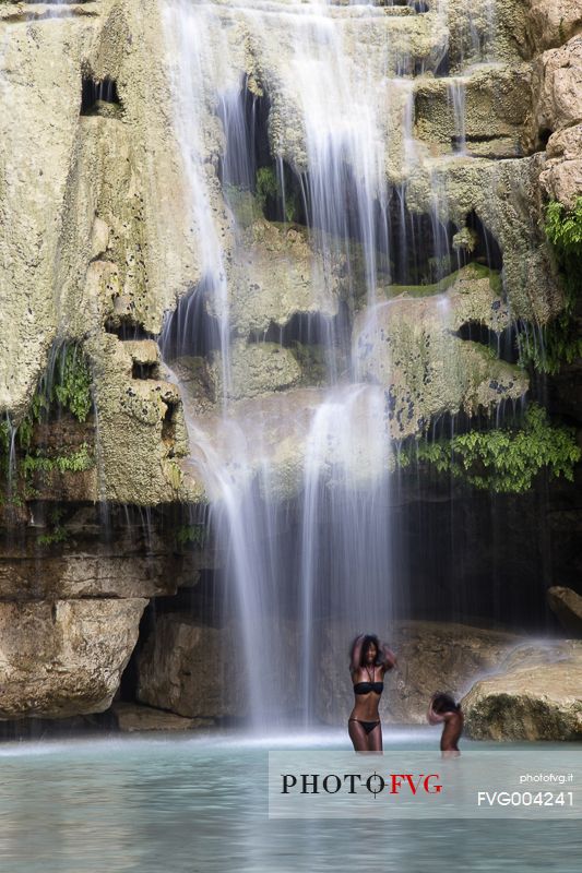 A girl having a shower under a waterfall along the course of the Tsiribina river