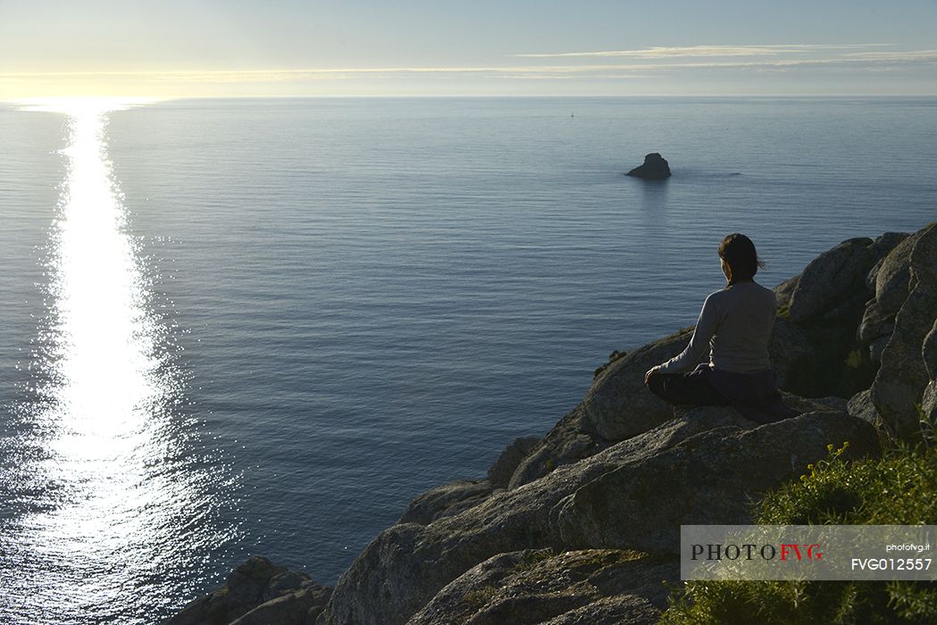 Young woman awaiting for sunset at Cape Fisterra or Finisterre, La Corua, Galicia, Spain, Europe