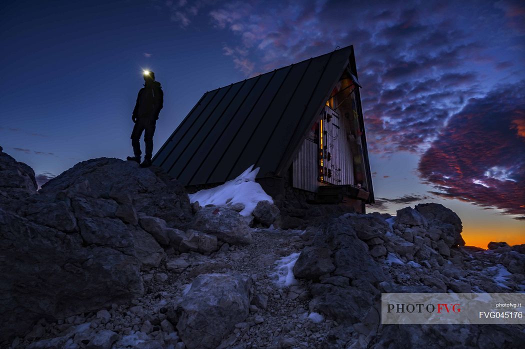 Hikers outside the Luca Vuerich bivouac at twilight, Foronon del Buinz, Montasio mountain range, Julian alps, Friuli Venezia Giulia, Italy, Europe