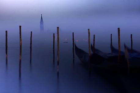 On a foggy winter morning, the bell tower of the San Giorgio island breaks through the fog while the gondolas sway slightly in the Venice lagoon, Venice, Veneto, Italy