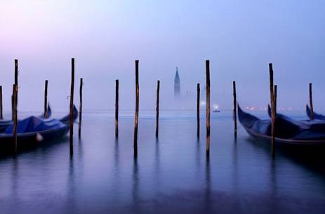 On a foggy winter morning, the bell tower of the San Giorgio island breaks through the fog while the gondolas sway slightly in the Venice lagoon, Venice, Veneto, Italy