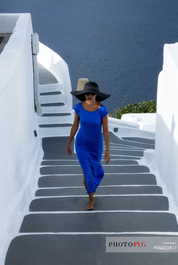 Lady in blue long dress walks on steps in Oia village, Santorini island, Greece
