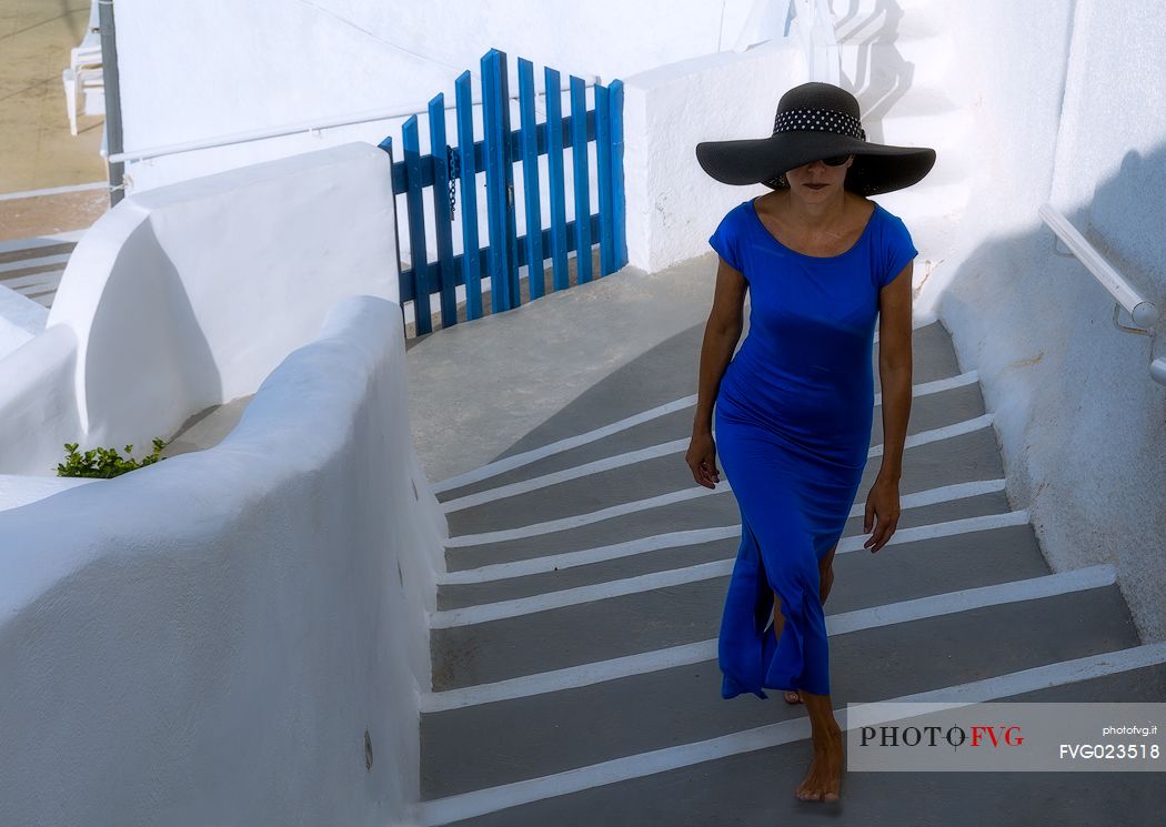 Lady in blue long dress walks on steps in Oia village, Santorini island, Greece
