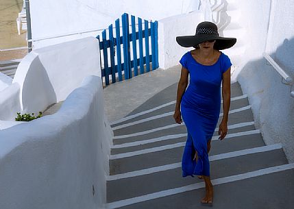 Lady in blue long dress walks on steps in Oia village, Santorini island, Greece
