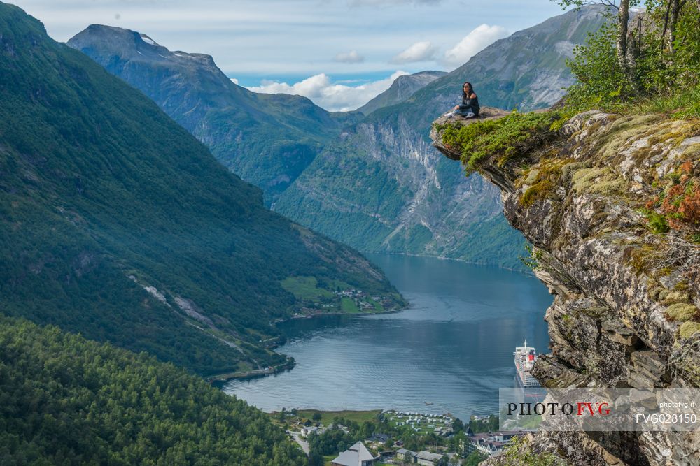 Girl relaxing on the Flydalsjuvet rock, over the Geiranger fjord, Norway