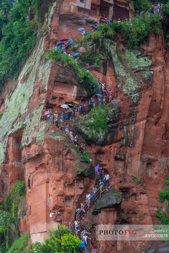 Tourists climb the cliff to admiring the Giant Buddha, the largest buddha of the world carved on Emei Shan, sacred mount, Leshan, Sichuan, China