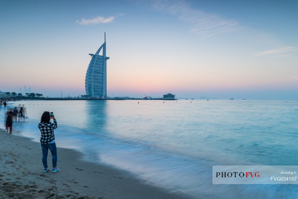 Tourist takes a picture at the Burj Al Arab Hotel from Jumeirah beach, at twilight Dubai, United Arab Emirates, Asia