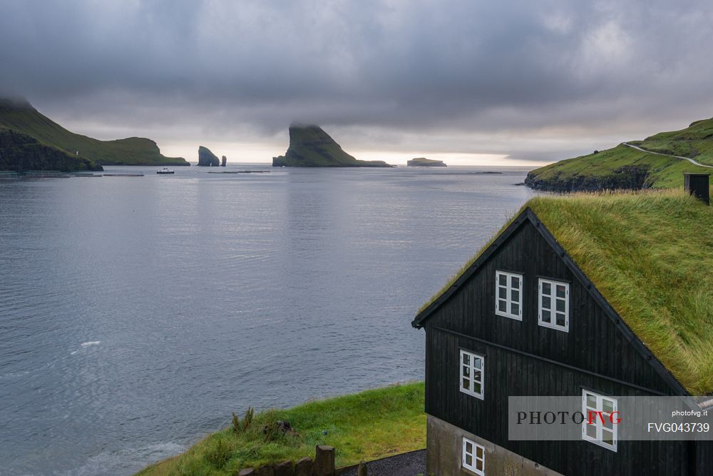 Traditional house in the village of Bur, near Srvgur, with the islet of Tindhlmuron the horizon, Vagar Island, Faeroe island, Denmark, Europe